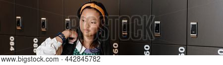 Asian brunette girl walking with backpack after class in checkroom at school