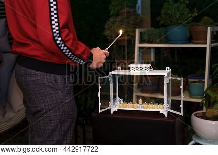 Young Jewish Man Lighting Menorah In Glass Boxes, Celebrating Hanukkah.lighting Menorah Outside Is A