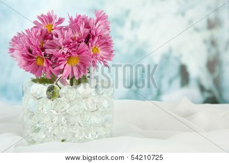 Beautiful flowers in vase with hydrogel on table on bright background