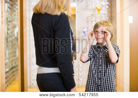 Preadolescent boy looking at mother while trying on spectacles in shop
