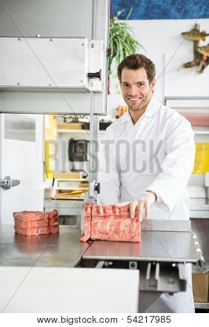 Portrait of happy butcher slicing meat on bandsaw at store