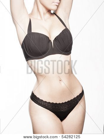 Close up view of the shapely curvaceous body of a sexy tanned young woman in black lingerie standing with her hands to her hips, torso view on white