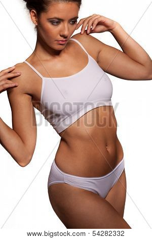 Close up view of the midriff torso of an athletic woman in a white sports bra and panties with a shapely curvy figure posing with her arms raised isolated on white