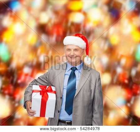 business, christmas, xmas, happiness concept - smiling old man in suit and santa helper hat with gift