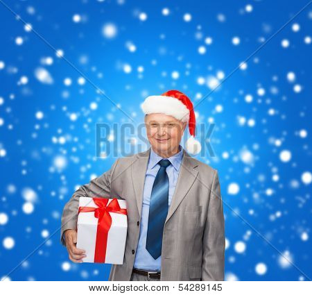 business, christmas, xmas, happiness concept - smiling old man in suit and santa helper hat with gift