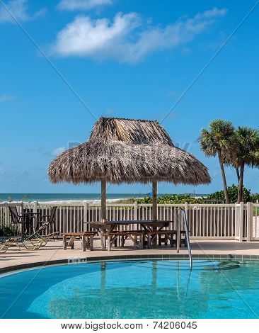 Beach table with hay parasol next to a swimming pool