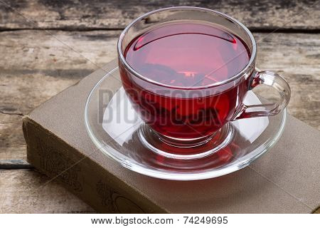 Cup Of Red Karkade Tea With Book On Wood Background