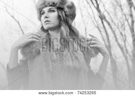 Girl in fur coat posing at branches background in black and white monochrome