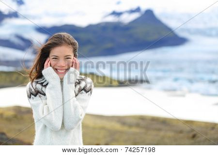 Asian woman portrait by glacier on Iceland wearing Icelandic sweater. Hiker tourist girl smiling cute in nature by glacial lagoon / lake of Fjallsarlon, Vatna glacier, Vatnajokull National Park.