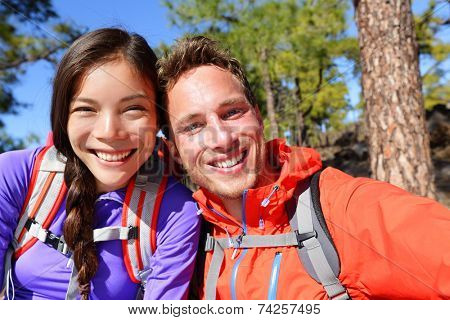Selfie couple taking self-portrait hiking using smart phone camera in nature. Happy couple taking self-portrait photo picture looking at camera smiling happy. Man and woman having fun together.