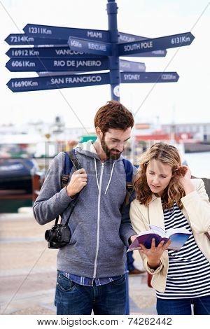 couple on travel holiday at sign with guide book