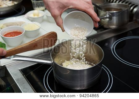 Chef is pouring rice in stewpan to cook risotto