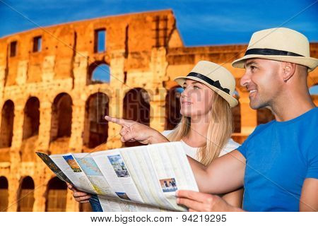 Beautiful active couple with map standing on Coliseum background and looking for right way, travel to Rome and exploring it by themselves, Italy Europe