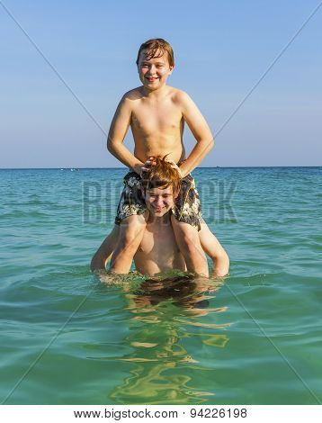 Brothers Are Enjoying The Clear Warm Water In The Ocean And Play Pickaback