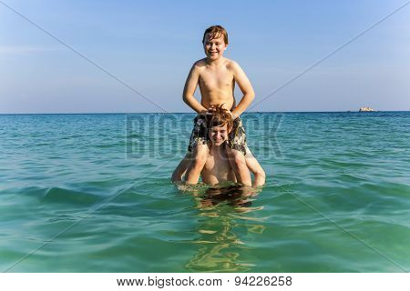 Brothers Are Enjoying The Clear Warm Water In The Ocean And Play Pickaback