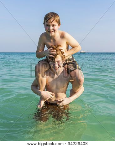 Brothers Are Enjoying The Clear Warm Water In The Ocean And Play Pickaback
