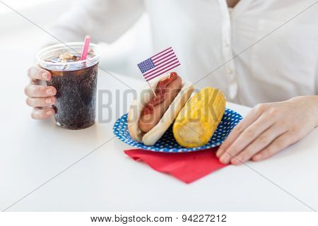 american independence day, celebration, patriotism and holidays concept - close up of woman hands with hot dog and corn holding coca cola drink in plastic cup on 4th july party