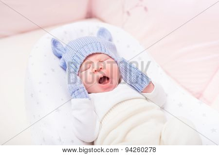 Yawning Little Baby Wearing Knitted Blue Hat With Ears And Mittens Lying In Beautiful Cradle
