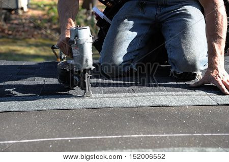 handyman using nail gun to install shingle to repair roof