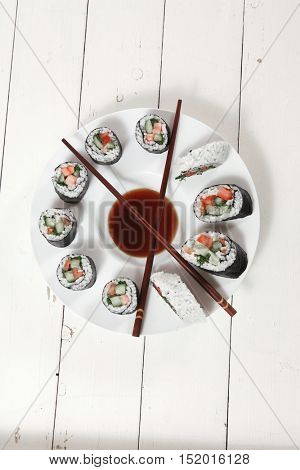 sushi maki rolls salmon with soy sauce and sticks on deep white plate on wooden table