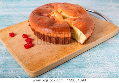 Home-made pie and several red berries nearby. Pie lies on a wooden board a blue table in rural style. From pie the piece is cut off.