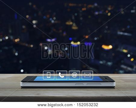 Telephone mobile phone at and email buttons on modern smart phone screen on wooden table in front of city tower background Customer support concept