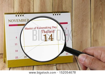 Magnifying glass in hand on calendar you can look Master of rainmaking DayThailand on 14 November concept of a public relations campaign in Technology and Innovation.