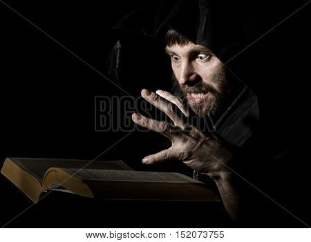 necromancer casts spells from thick ancient book by candlelight on a dark background.