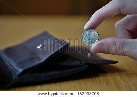 Male hand holding a silver Russian Rouble coin (currency in Russia, Russian Ruble or Rouble, RUB) and withdrawing that from the brown leather wallet