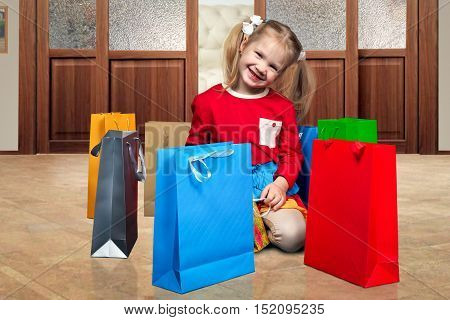Happy little gHappy little girl and a lot of shopping bags. A child on the floor in the apartment. Shopping bags colorful brightirl and a lot of shopping bags. A child on the floor in the apartment. Shopping bags colorful bright