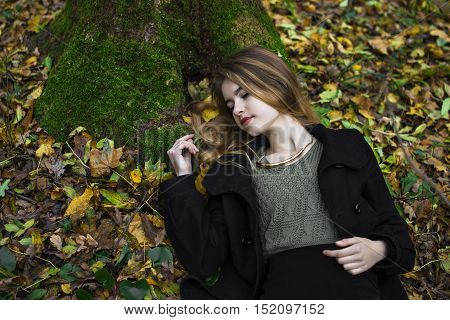 Young beautiful girl in blue jeans lying on yellow leaves, view from above, in the autumn park