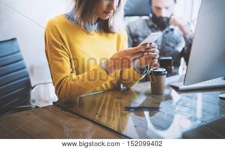 Working process in modern office.Woman looking to her mobile phone and sitting at the wooden table.Man typing on his smartphone.Horizontal photo, blurred background
