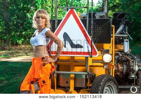 Sexy woman worker in overalls. Road sign on the background.