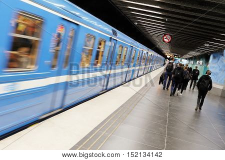 Stockholm, Sweden - May 7, 2015: Interor of the subway station Stadion in the Stockholm Metro. People walking on the plattform to the exit while a blue train leaving the station heading for Morby Centrum.