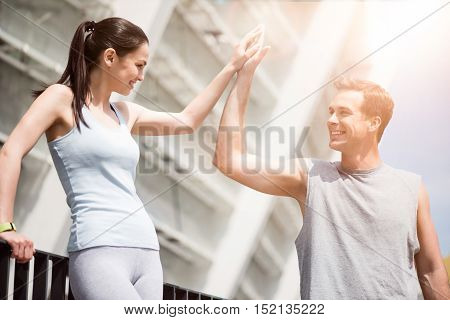 Greetings after exercises. Beautiful slim woman and a fit man smiling and high fiving each other after training outdoors.
