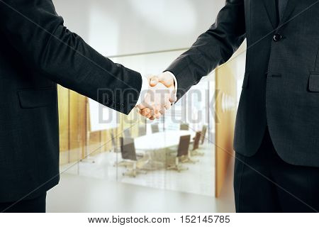 Close up of businessmed shaking hands on office interior background. Partnership concept
