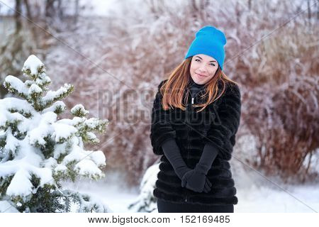 Portrait of pretty attractive girl in a fur coat and gloves in the winter park. Winter fun. Walks in the open air.
