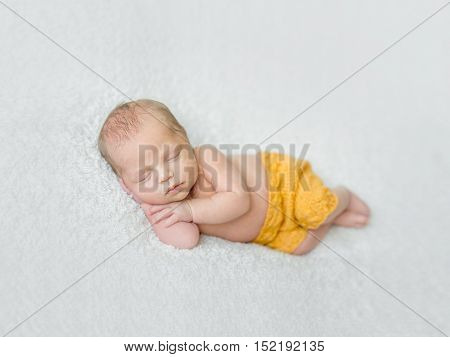 sweet sleeping newborn boy in yellow panties with head on his hand