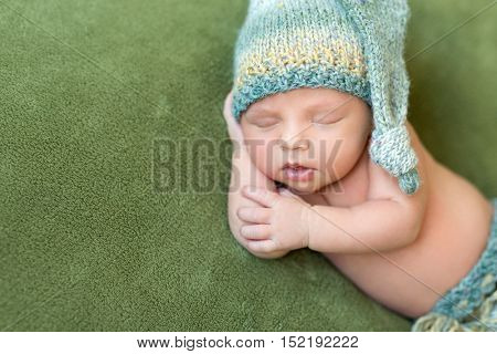 funny newborn baby in knitted hat sleeping with opened mouth on green blanket