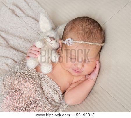sweet sleeping infant girl with headband and toy in hand covered with warm shawl