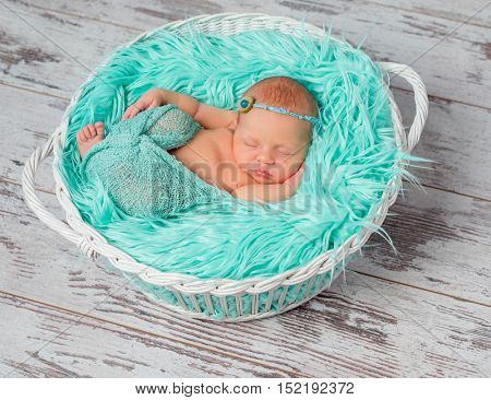 lovely sleeping newborn girl in round cot with turquoise fluffy blanket