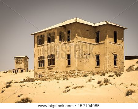 Ghost buildings of old diamond mining town Kolmanskop near Luderitz in Namibia. Abandoned house ruins sunken in the sand dunes of Namib Desert. Vintage toning photography.