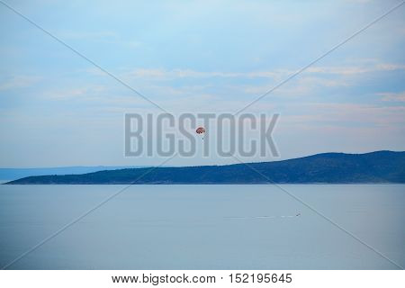 Beautiful blue sea and sky horizon with red parachute and parachutist flying on seascape