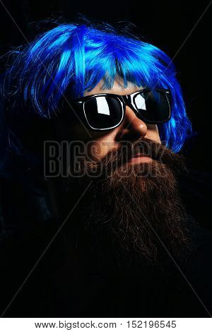 Handsome man hipster fashion model with long brunette beard with moustache in sunglasses and blue wig on black background
