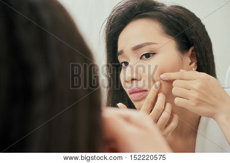 Young woman popping pimple on her check