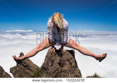 Young blonde woman acrobat making splits on rock on mountain's summit.