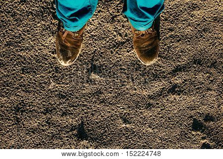 Male shoes on textured sand contrast blue trousers.