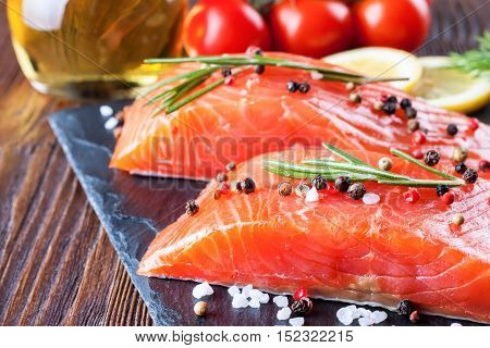 Raw salmon fillet and ingredients for cooking on a slade board and brown wooden background.