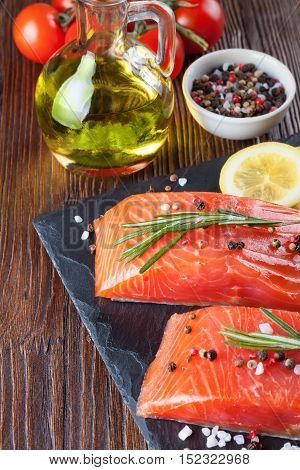 Raw salmon fillet and ingredients for cooking on a slade board and brown wooden background.
