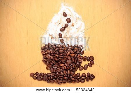 Cappuccino time. Roasted coffee beans placed in shape of cup and saucer with cinnamon white froth on wooden surface background